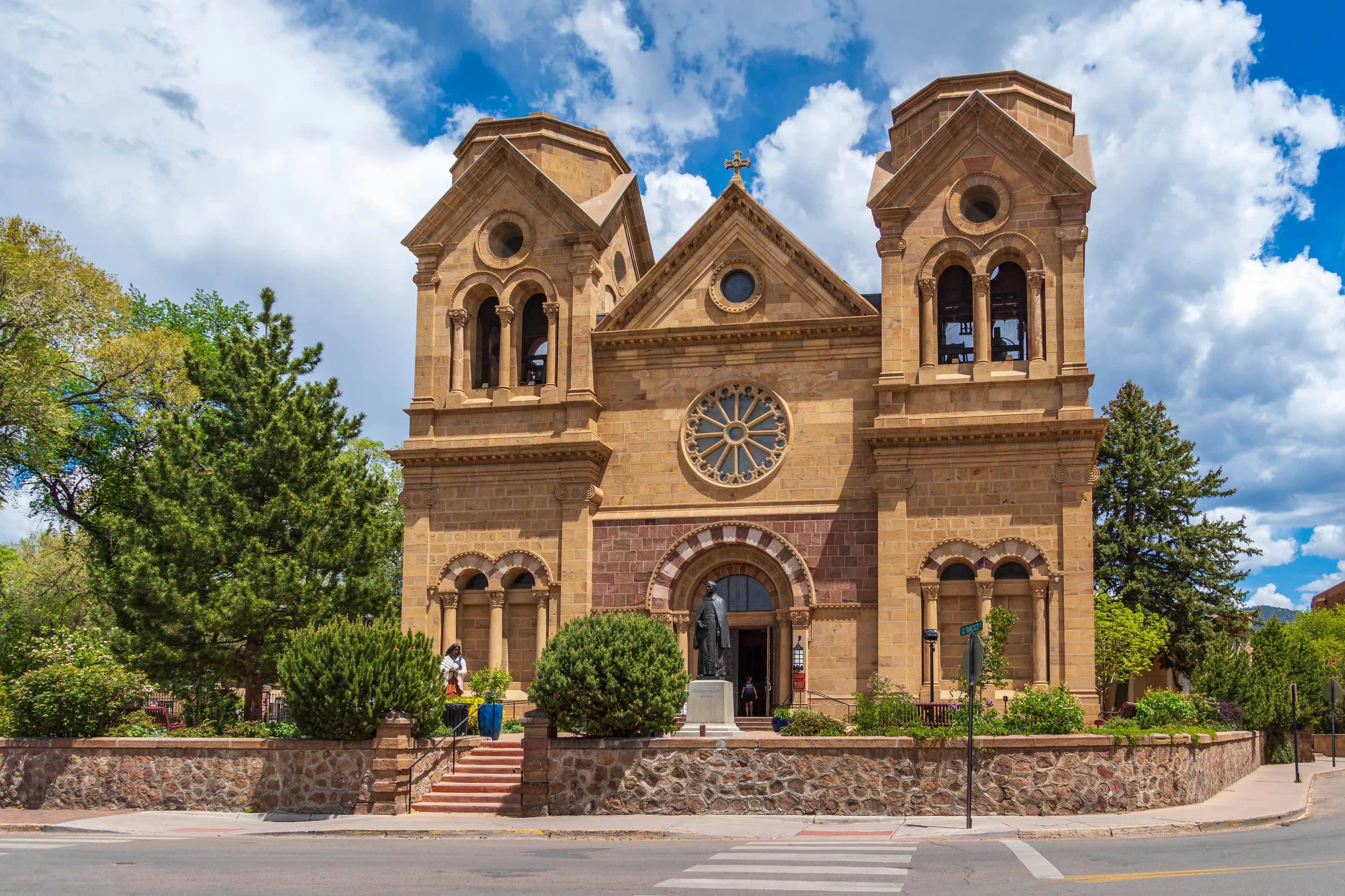 The Cathedral Basilica of St. Francis of Assisi in Santa Fe, its sandstone towers and rose window under a blue sky with white clouds
