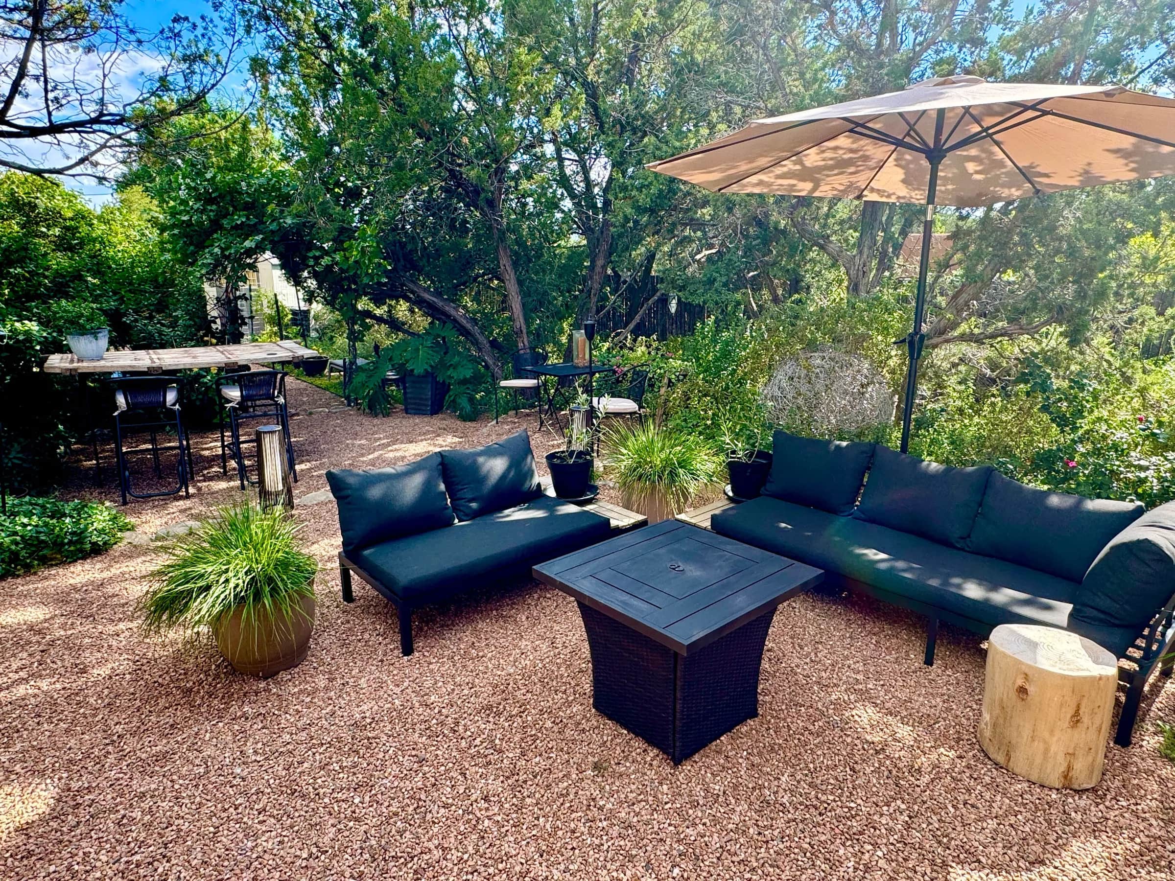 The Birdsong garden lounge: dark sofas around a fire table under an umbrella, a bar table and the gardens beyond