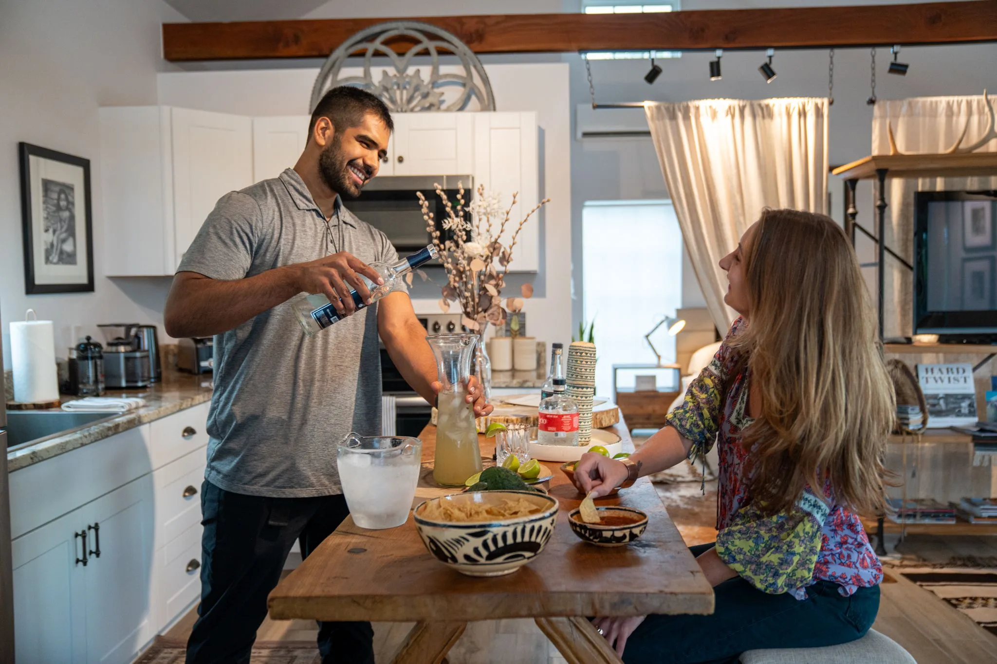 In the Farmhouse 1 kitchen, a man pours tequila into a pitcher of margaritas while a woman laughs across the counter