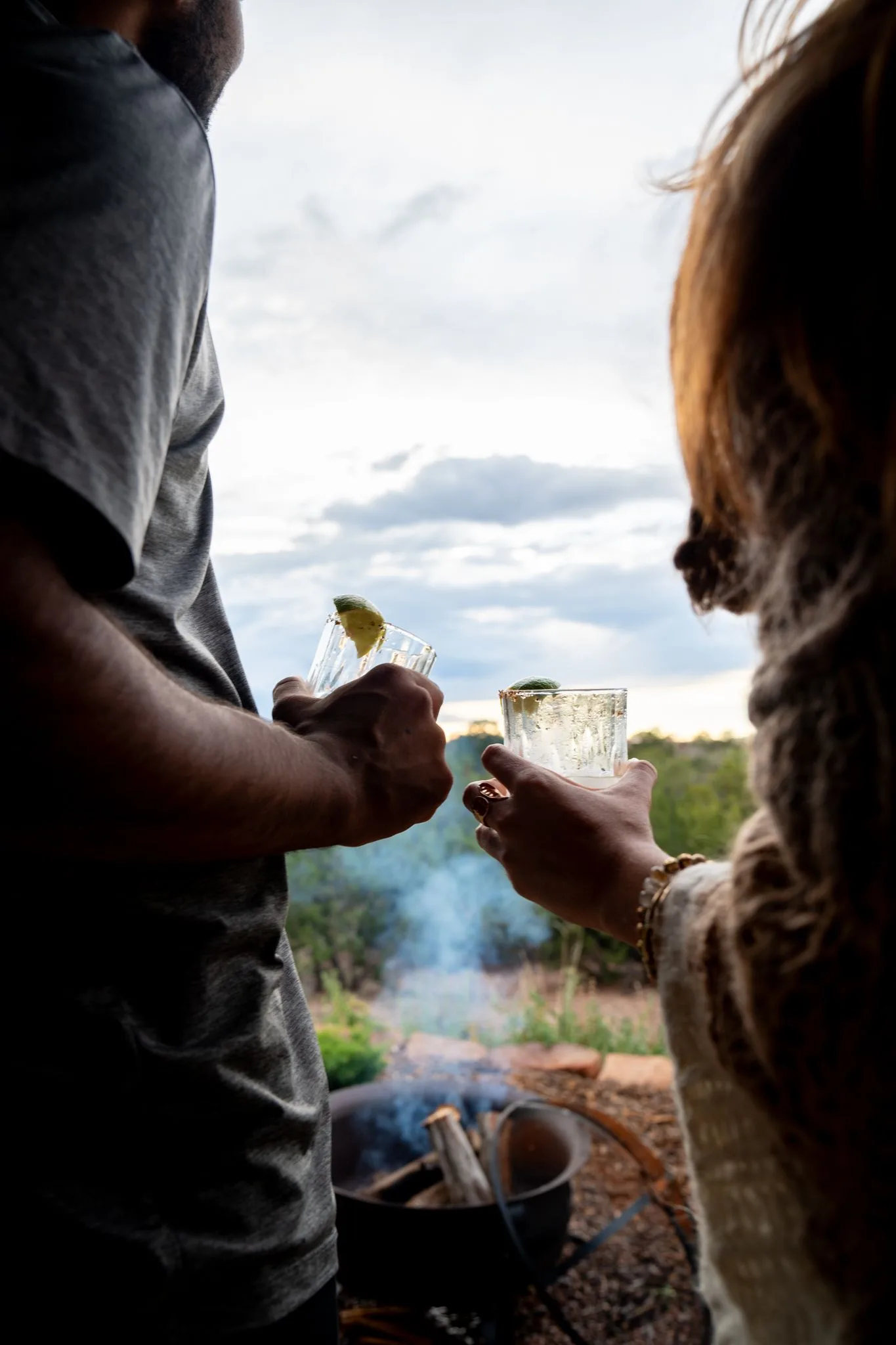 Two guests raise margaritas at dusk, the fire smoking in the garden beyond the portale
