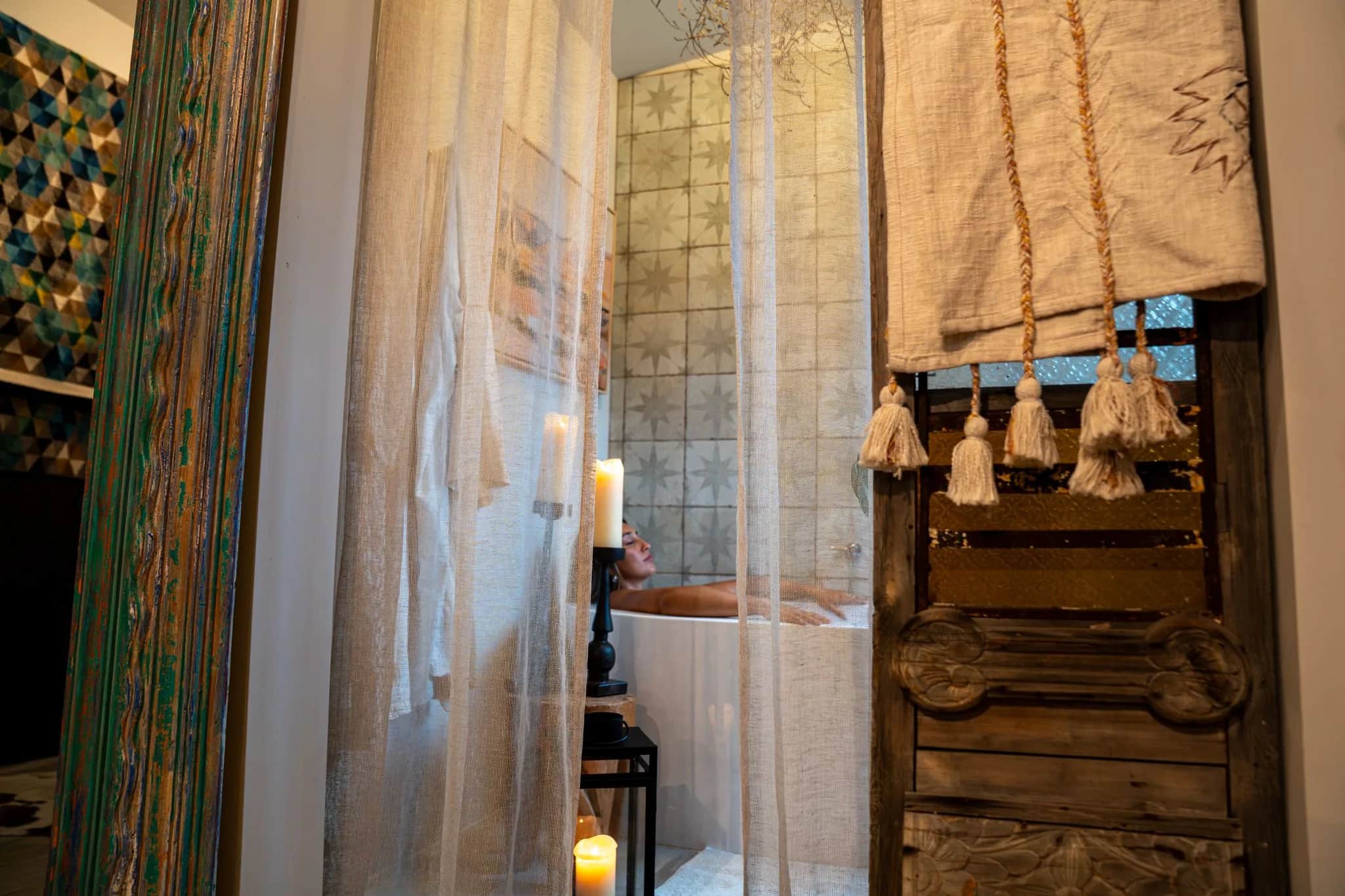 The Farmhouse 2 soaking room through sheer curtains and a carved screen, a deep white tub and lit candles