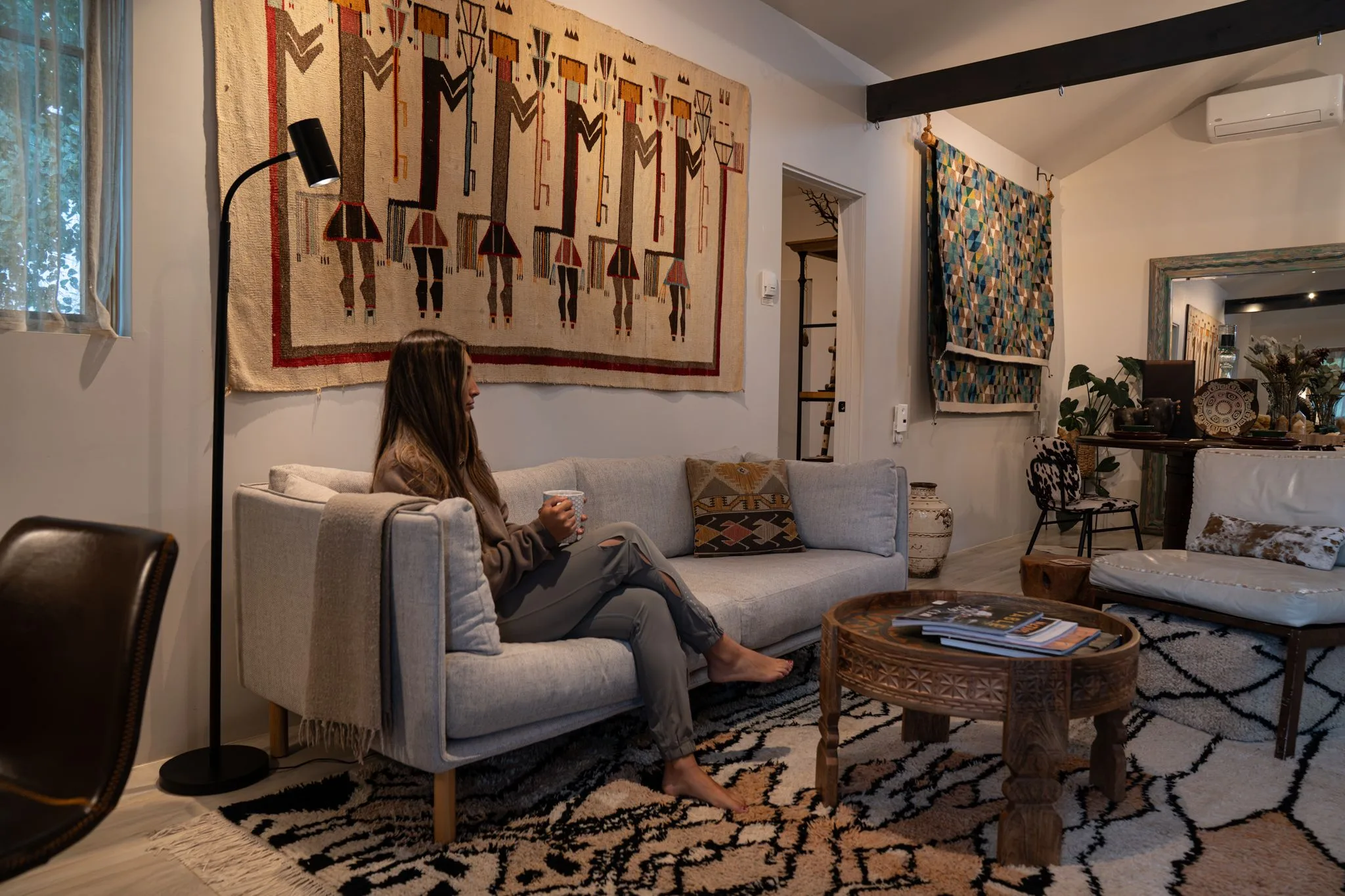 A guest curled on the Farmhouse 2 sofa with a mug, a large weaving on the wall above
