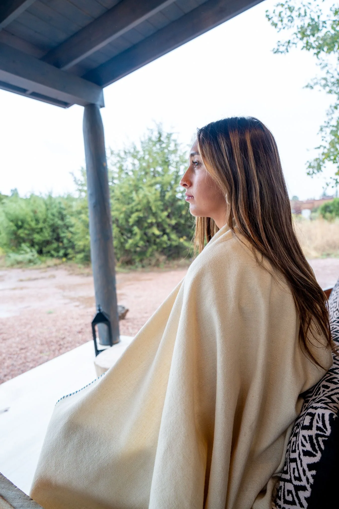 A guest wrapped in a cream blanket looks out from the porch across the land