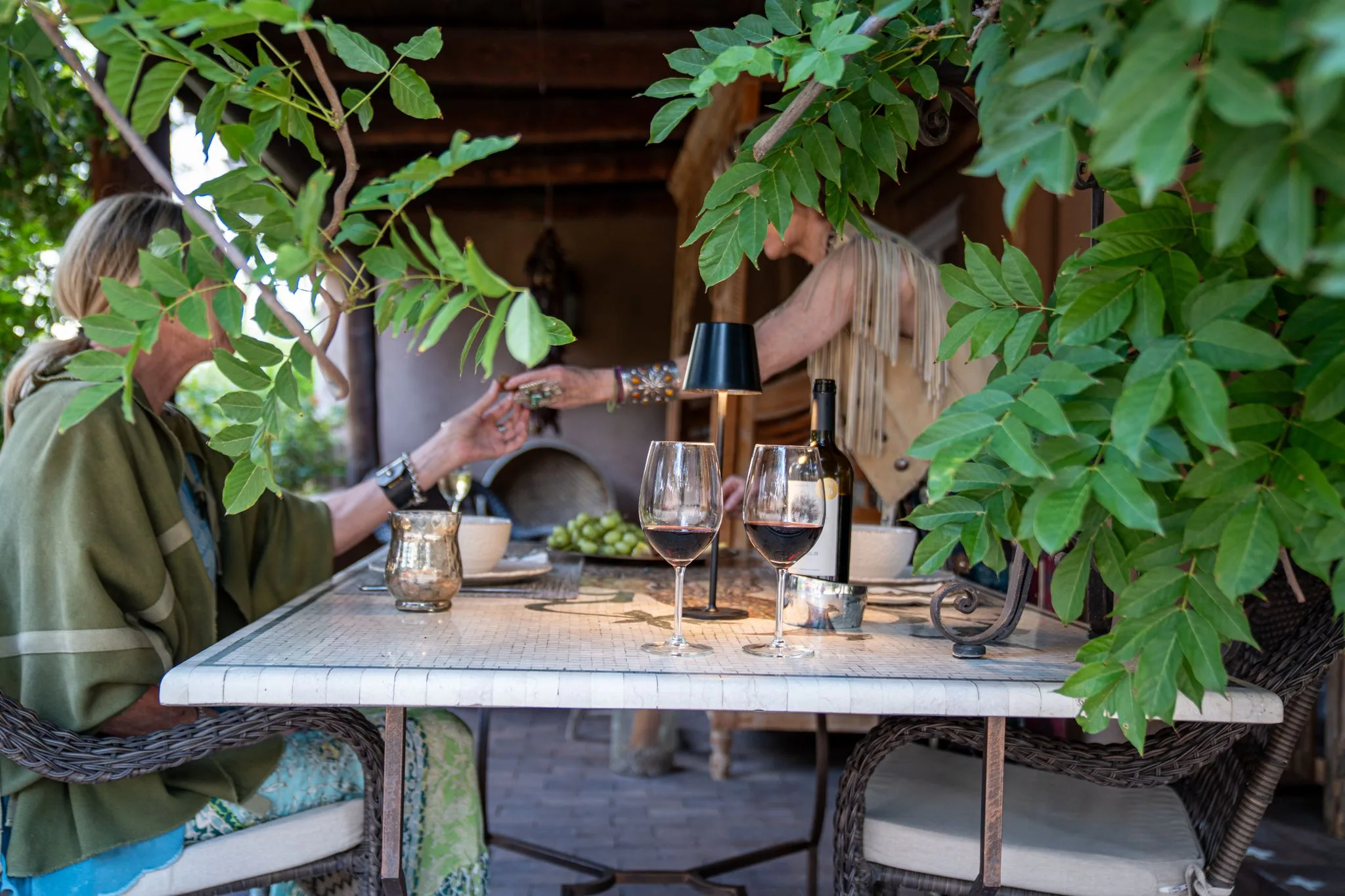Two guests share red wine at the mosaic table under the vines on the Los Santos portale