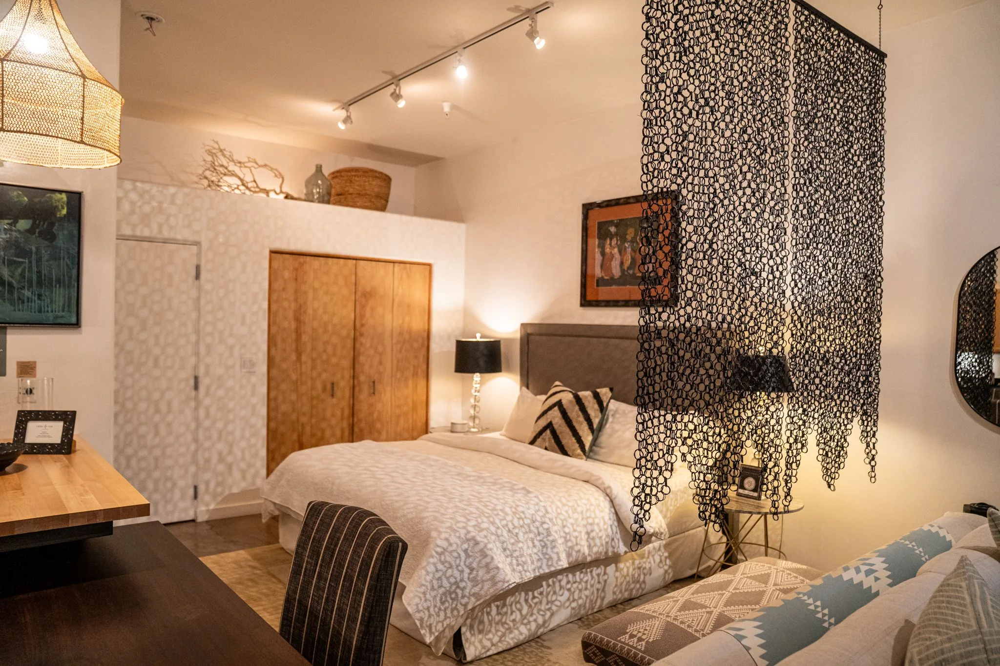 A king bed with white linen and black lamps behind a hanging screen of dark links