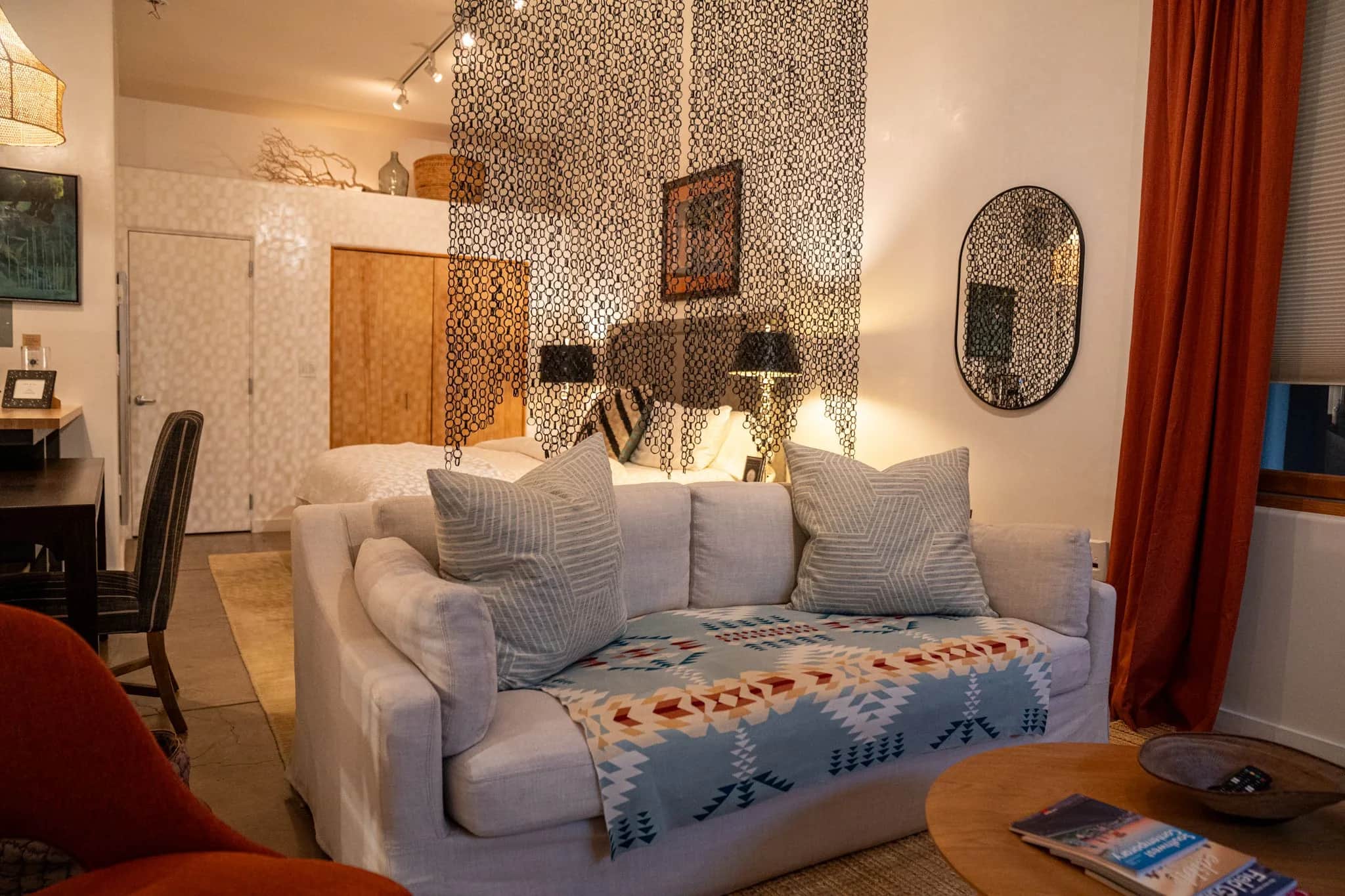 A white slipcovered sofa with a woven throw in front of a hanging screen of dark links