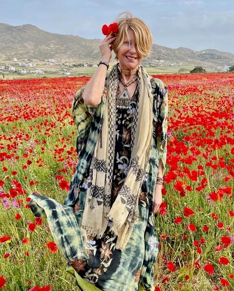 Kris Lajeskie in a field of red poppies, a poppy in her hair, wearing a green and indigo kimono and silver jewelry, hills and white houses behind her