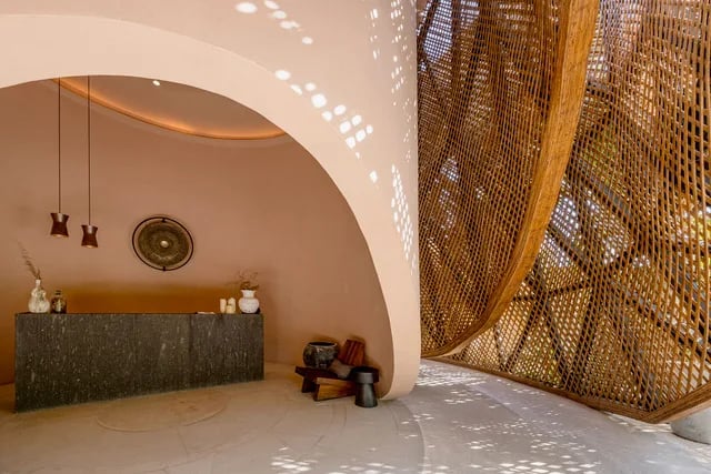 The Aflora lobby: a curved plaster arch and a woven wooden lattice over a dark stone reception desk, light falling through in dots