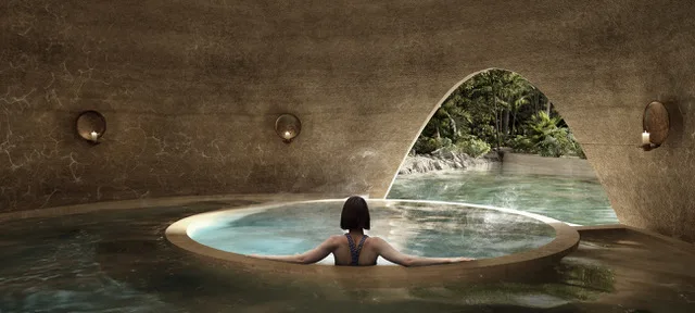 A guest in a round salt water pool inside a stone cave, an arched opening to the jungle beyond