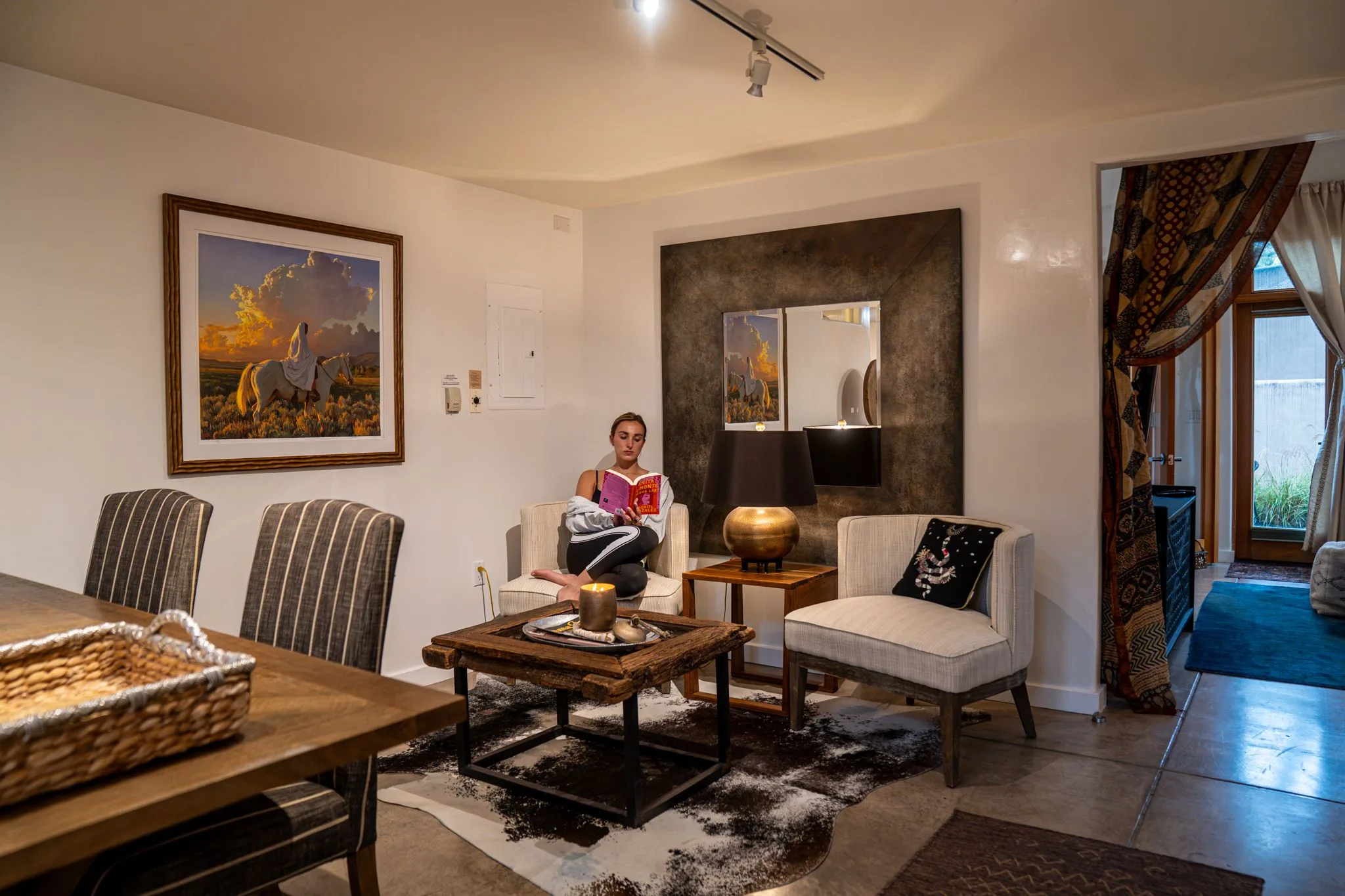 A guest reading in a white armchair in the sitting corner, lamplight on the bronze mirror