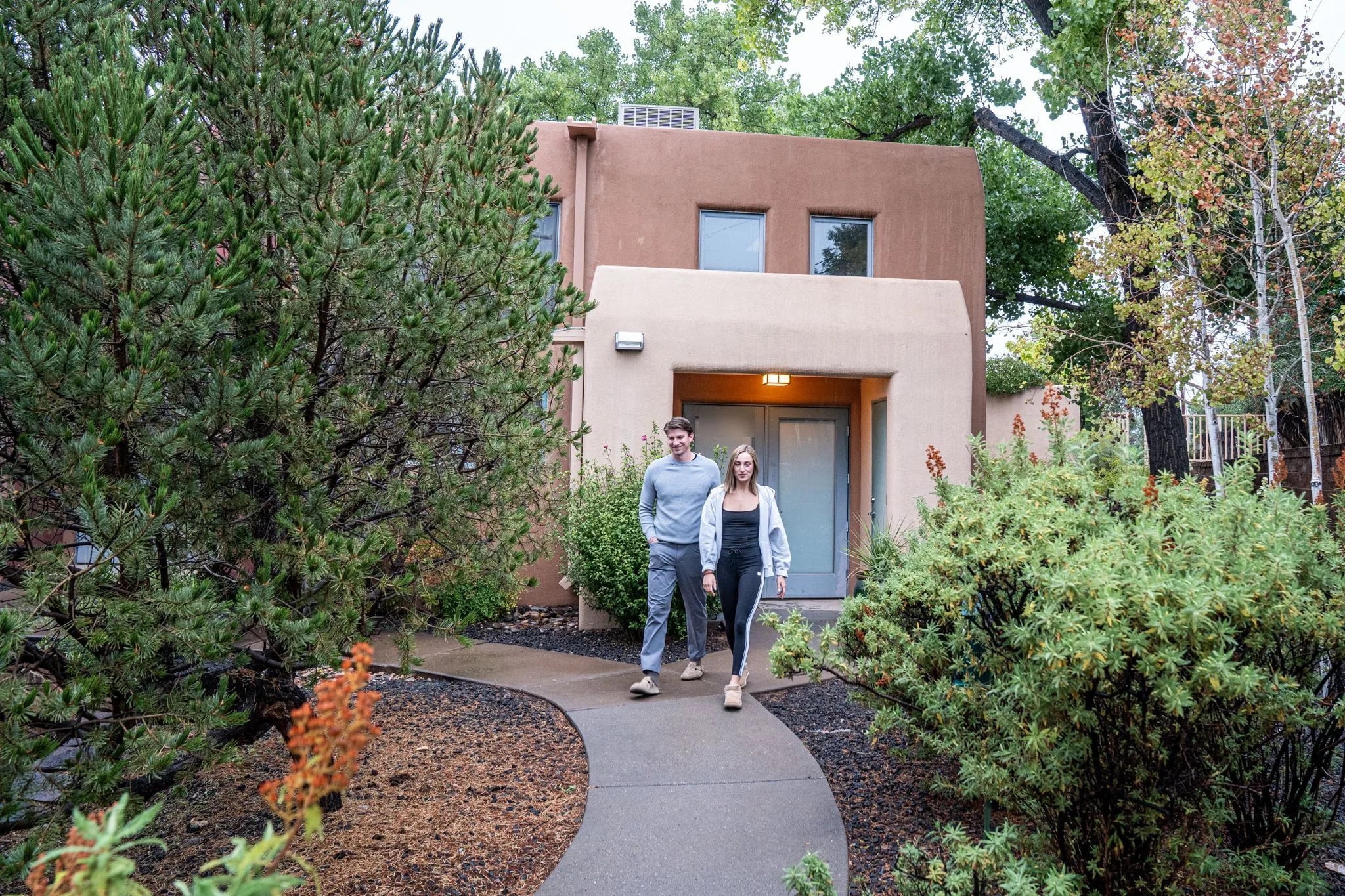 A couple walks out along a curving path from Tumbleweed between junipers and wildflowers