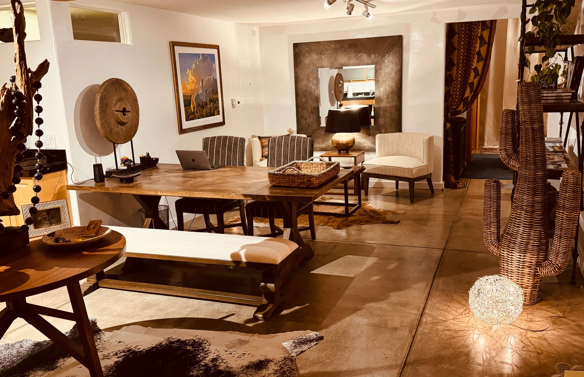 The Tumbleweed great room: a long wood dining table with a bench and striped chairs, white armchairs and a bronze mirror beyond, a cowhide on the concrete floor
