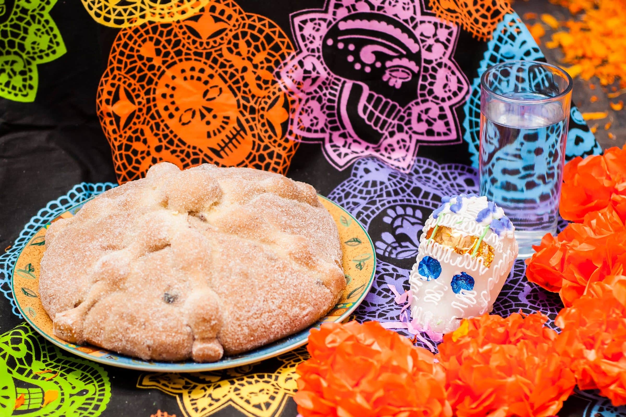 An ofrenda with pan de muerto, a sugar skull, marigolds, and cut paper banners
