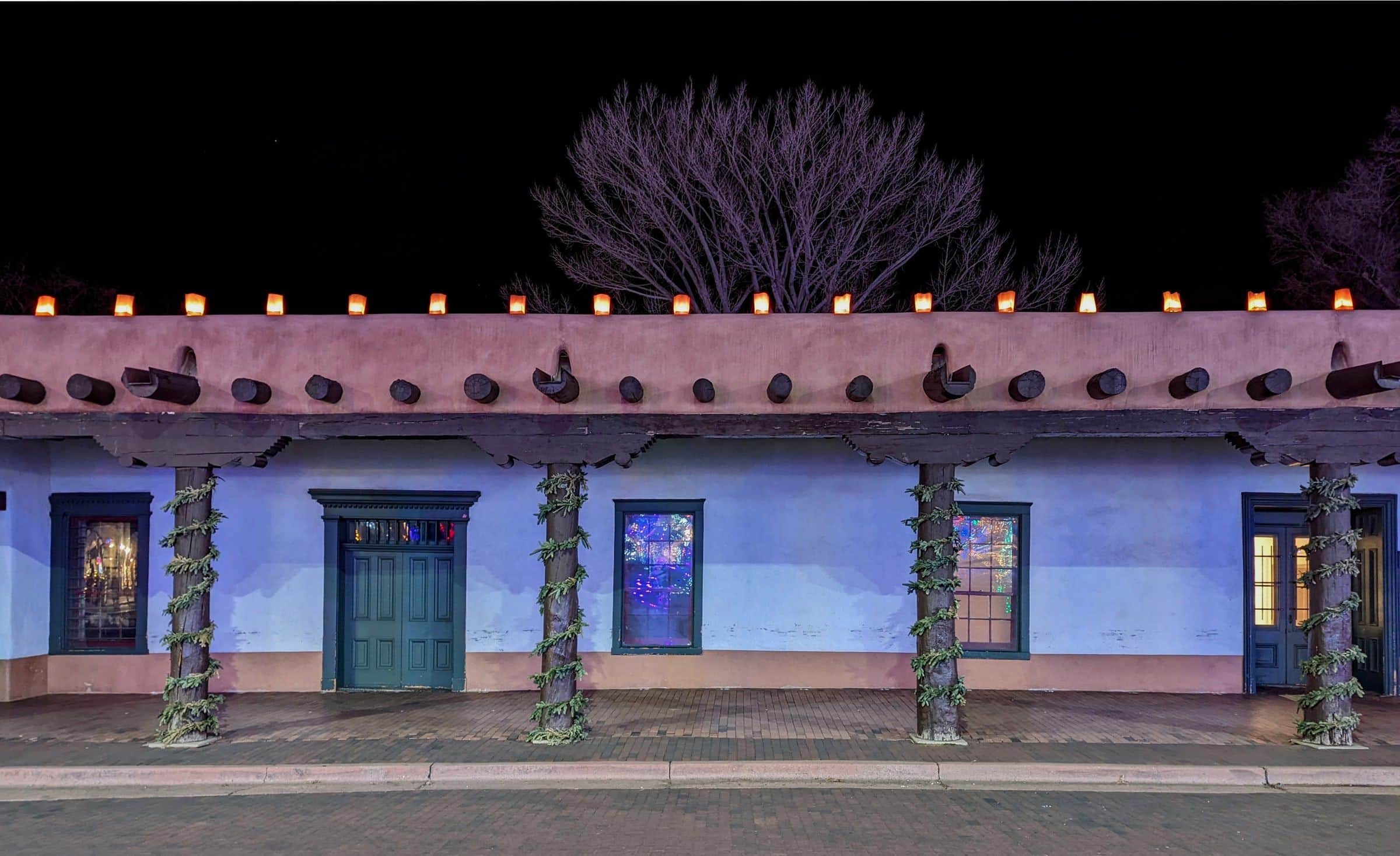 Farolitos along the roofline of the Palace of the Governors at night, its portal hung with garlands
