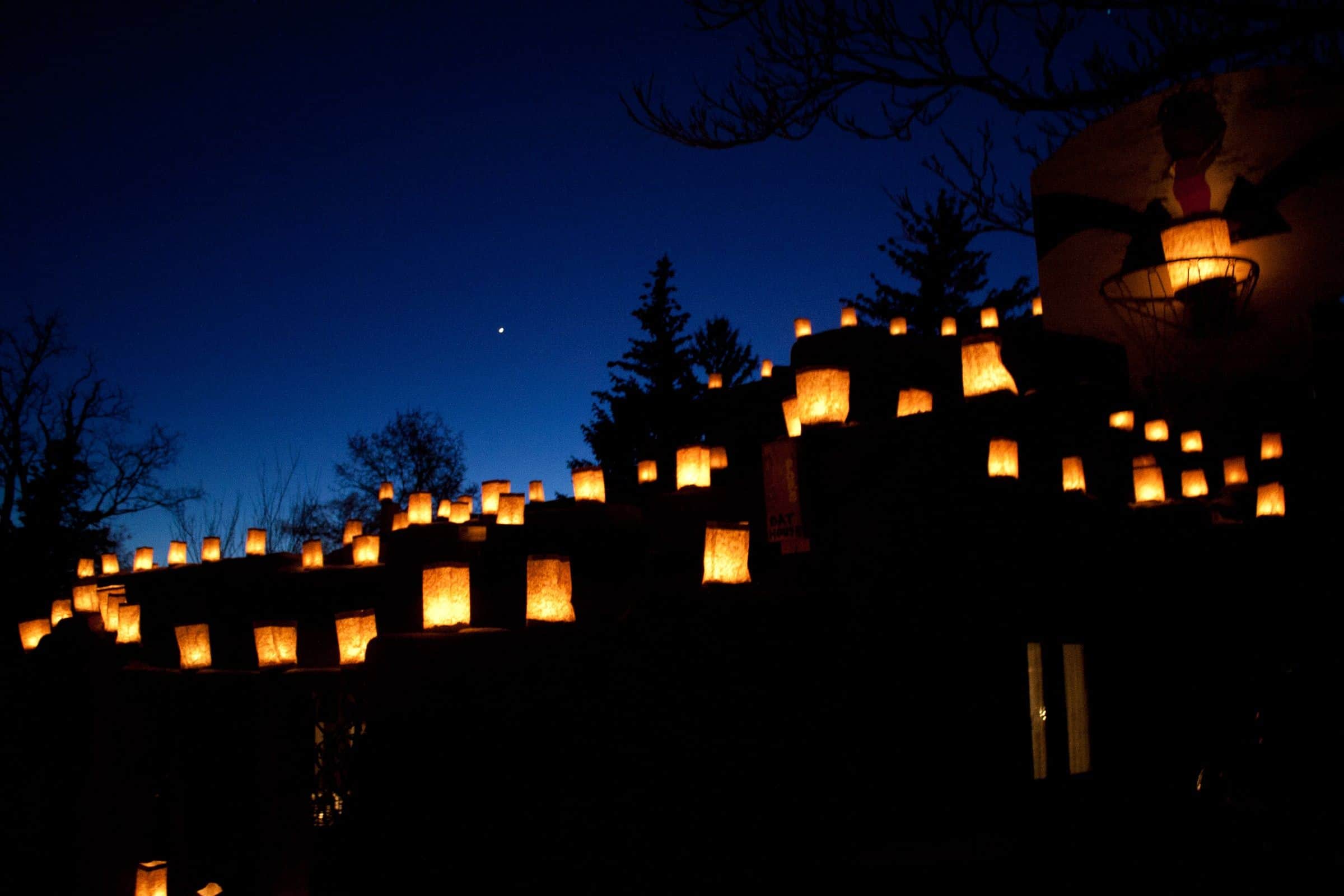Glowing farolitos lining the walls and rooftops of Santa Fe adobes at dusk