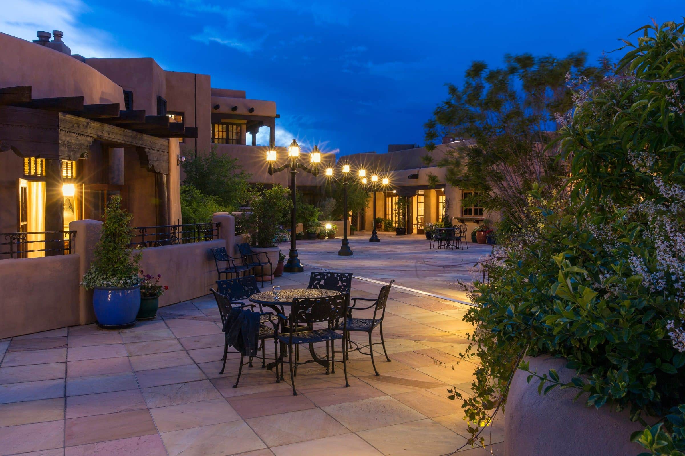 The terrace of La Fonda on the Plaza at dusk, lanterns lit along the adobe walls