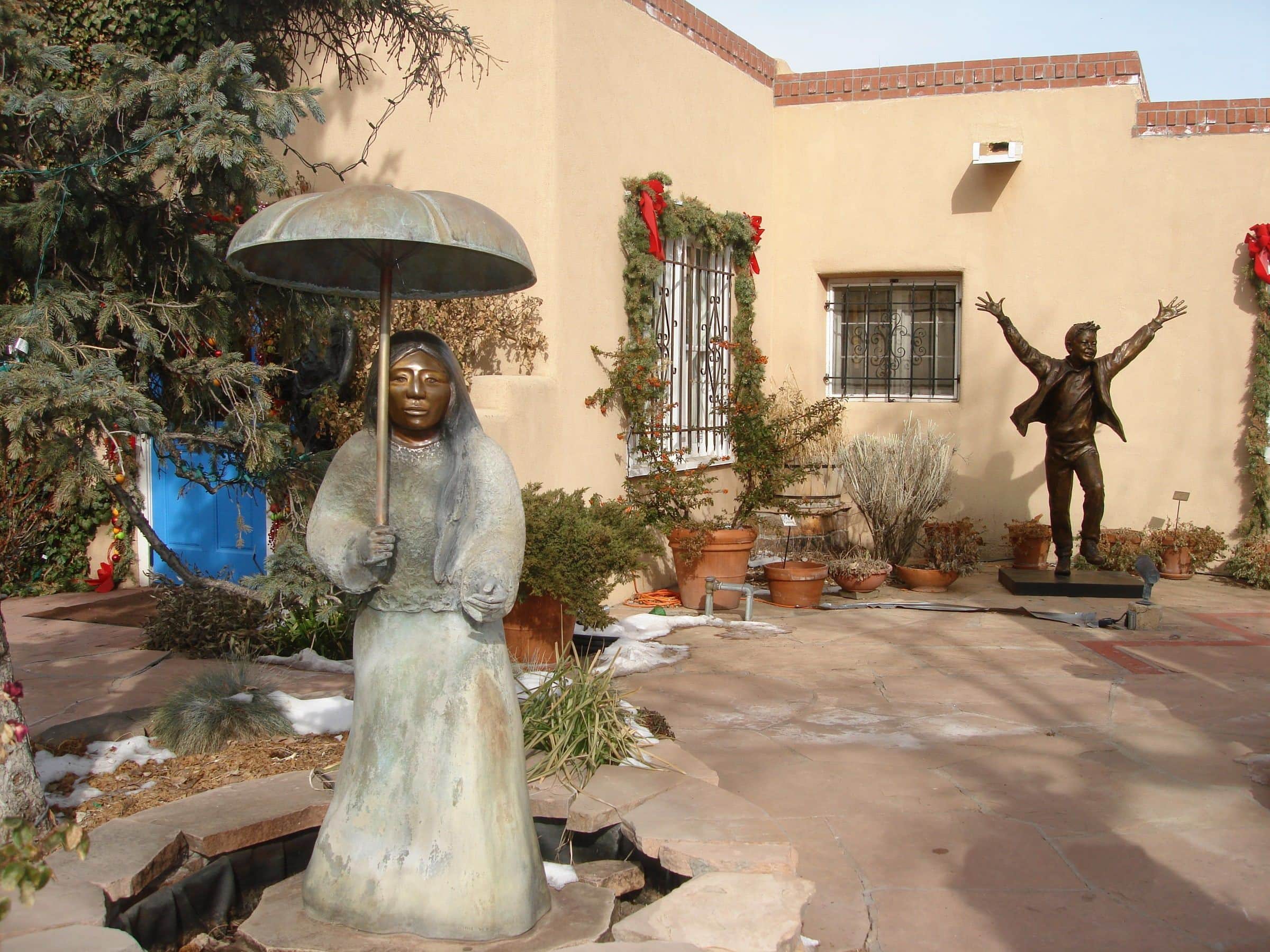Bronze sculptures in a gallery courtyard on Canyon Road, adobe walls and a wreath behind them